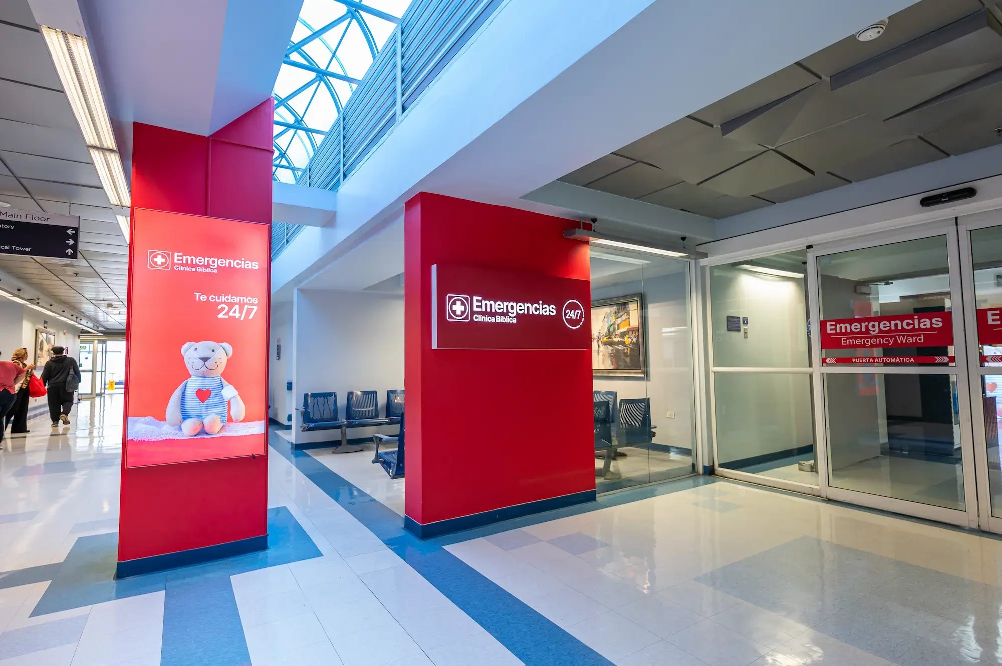 Entrada principal a la sala de Emergencias 24/7 del Hospital Clínica Bíblica, mostrando los rótulos informativos en la zona de acceso.