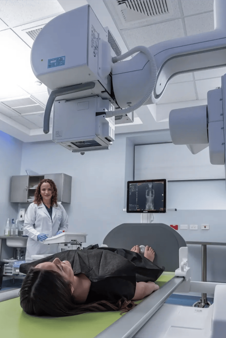 Radiology specialist at Hospital Clinica Biblica operating a Philips robotic digital X-ray and fluoroscopy system for a patient's diagnostic study.
