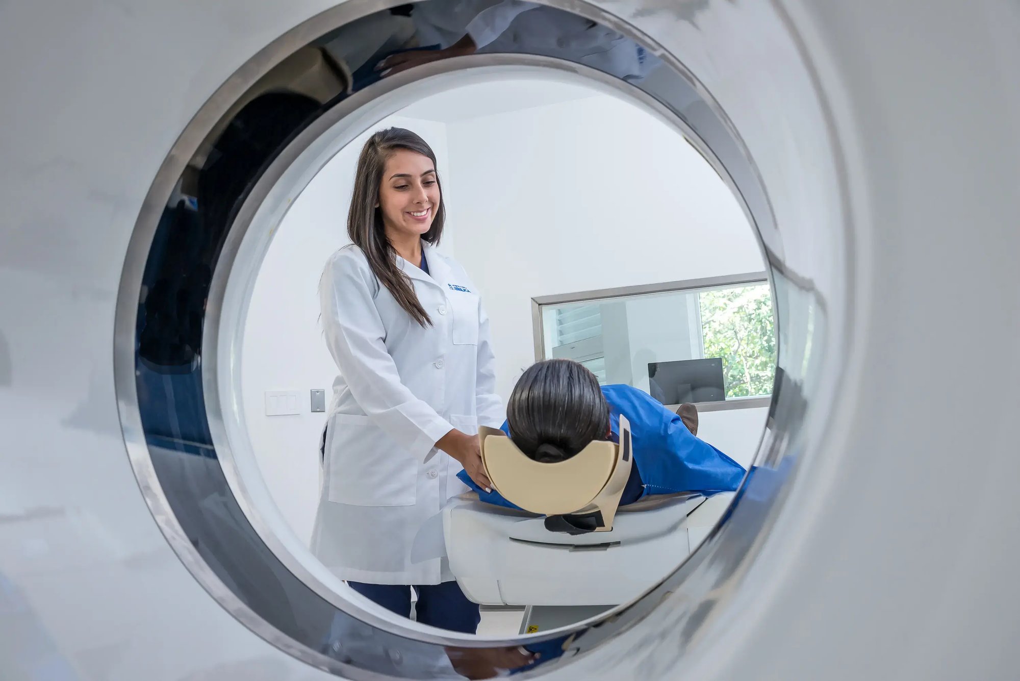 View through a CT scanner machine at Hospital Clinica Biblica showing a radiology specialist preparing a patient for a computed tomography scan.