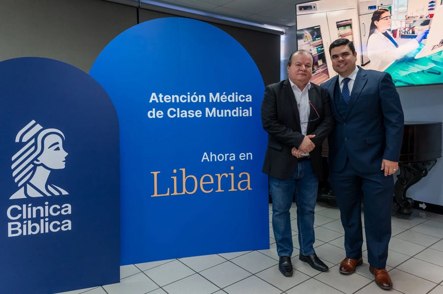 Dos hombres posan junto a panel promocional de Clínica Bíblica en Liberia