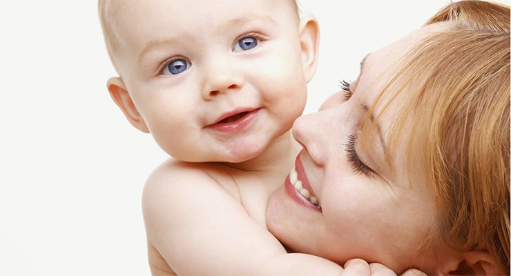 Madre sonriente sosteniendo en brazos a su bebé mientras lo mira de cerca