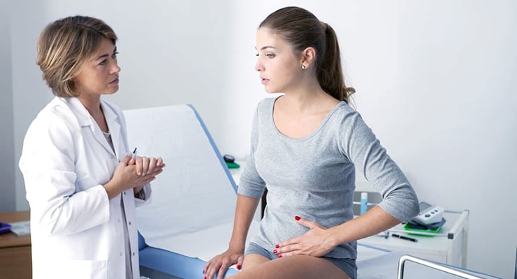 Médica conversando con una paciente sentada en una camilla durante una consulta ginecológica