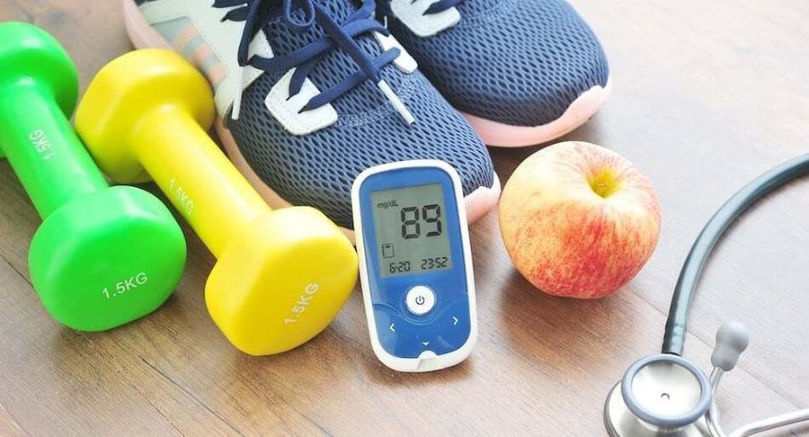 Elementos para control de la diabetes: glucómetro, pesas, tenis, manzana y estetoscopio