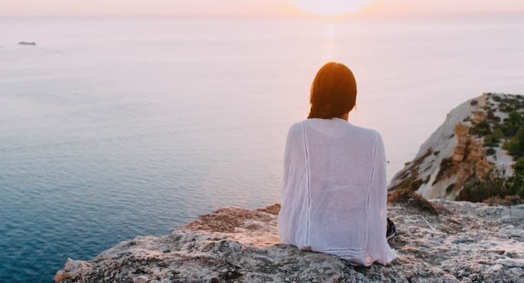 Mujer sentada frente al mar al atardecer en actitud de reflexión