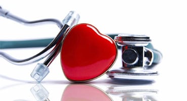 Corazón rojo decorativo junto a un estetoscopio sobre superficie blanca