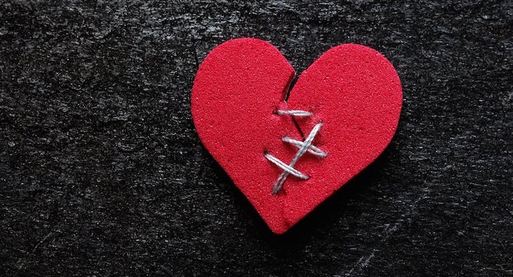 Corazón rojo de tela cosido con hilo blanco sobre fondo oscuro