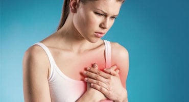 Mujer joven sosteniendo su pecho con expresión de dolor intenso, ilustrando los síntomas de un posible infarto o afección cardiovascular.