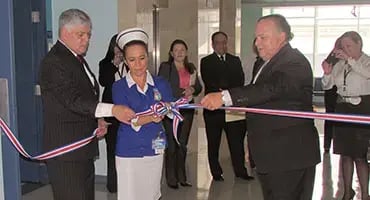 Acto de corte de cinta realizado por dos hombres y una enfermera durante una inauguración en un edificio.