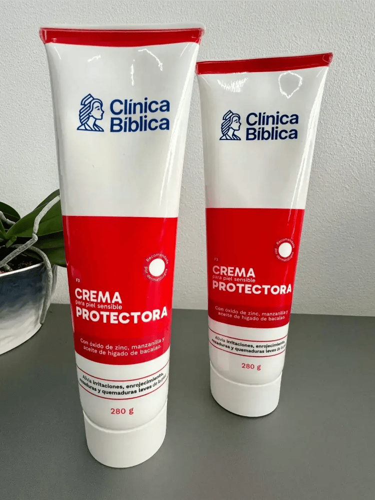 Dos tubos de crema protectora Clínica Bíblica sobre una mesa gris con empaque blanco y rojo