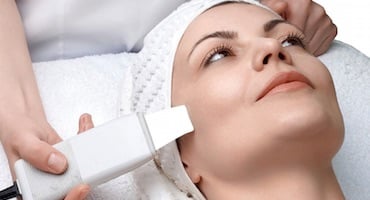 Especialista realizando un tratamiento de limpieza facial profunda a una paciente, utilizando equipo profesional para el cuidado de la piel.