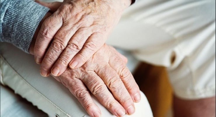 Manos de persona adulta mayor apoyadas sobre sus piernas