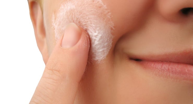 Primer plano de una persona aplicando una crema hidratante blanca en su mejilla con el dedo, representando el cuidado de la piel.