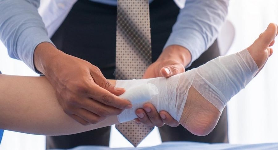 Primer plano de un profesional médico vendando cuidadosamente el tobillo de un paciente para el tratamiento de una úlcera o lesión cutánea.