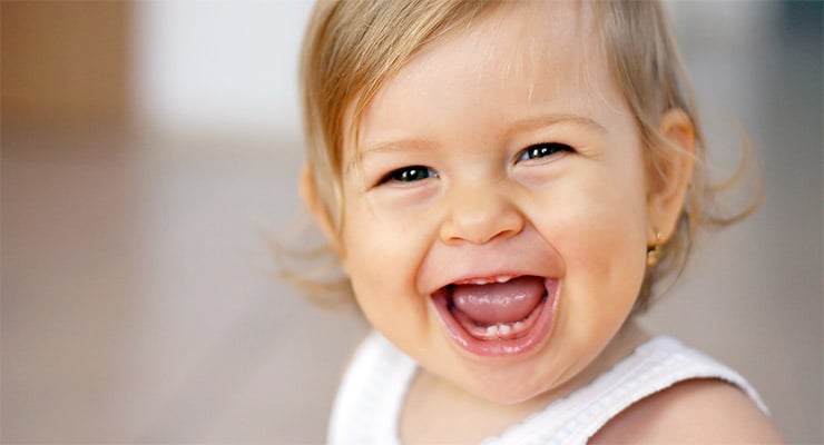 Bebé sonriendo con primeros dientes visibles durante la dentición infantil
