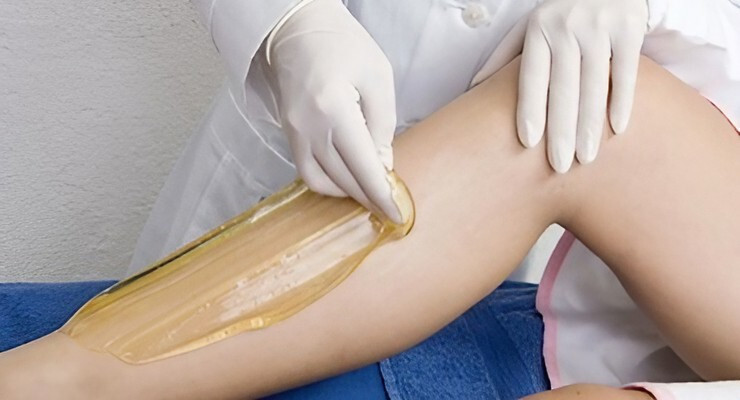 Aplicación de cera para depilación en pierna con guantes médicos