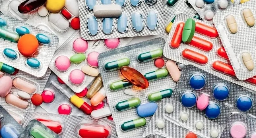 Vista detallada de diversos blísters con pastillas y cápsulas de diferentes colores esparcidas, representando medicamentos en desuso o vencidos.