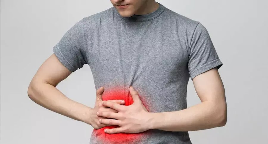 Hombre con dolor abdominal intenso sosteniendo el estómago con zona enrojecida