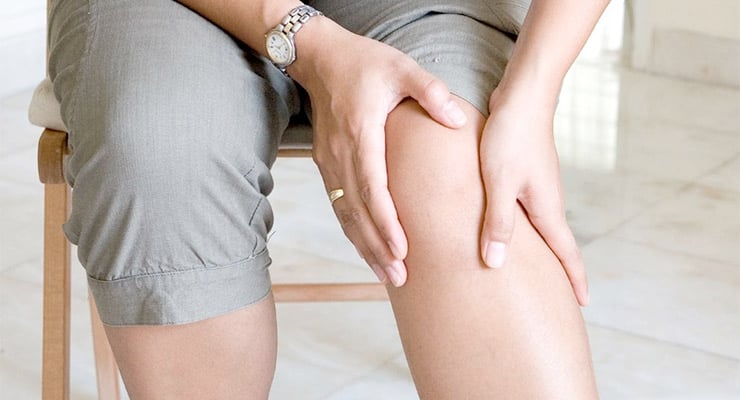 Persona sentada tocándose la rodilla con ambas manos en señal de dolor articular.