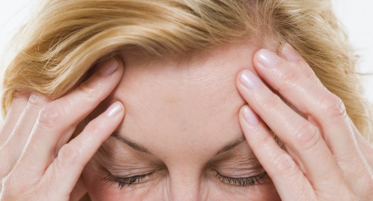 Mujer con los ojos cerrados presionando su cabeza con ambas manos en gesto de dolor o malestar