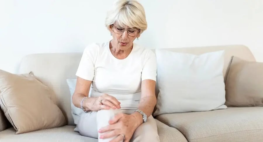 Mujer adulta mayor sentada en un sofá con dolor en la rodilla
