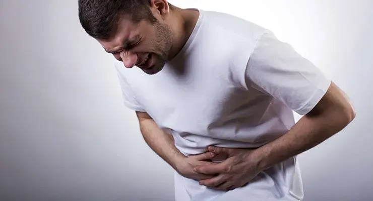 Hombre sujetando su abdomen con gesto de dolor por malestar estomacal.