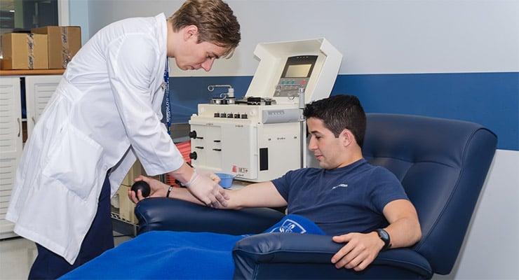 Profesional de salud realizando una extracción de sangre a un donante en una sala de banco de sangre.