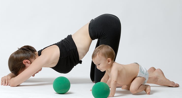 Mujer realizando ejercicio en el suelo junto a un bebé que gatea, ambos apoyados con las manos y rodillas.