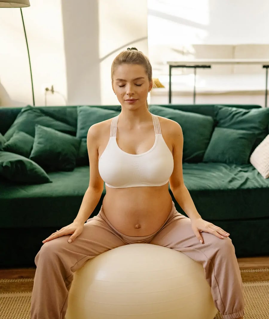 Mujer embarazada haciendo ejercicios prenatales sobre pelota de pilates en casa