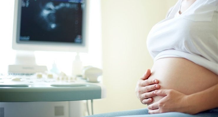 Mujer embarazada sosteniendo su vientre durante una consulta médica con equipo de ultrasonido al fondo