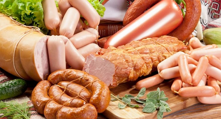 Variedad de embutidos y carnes procesadas como salchichas, jamón y chorizos sobre una tabla de madera.