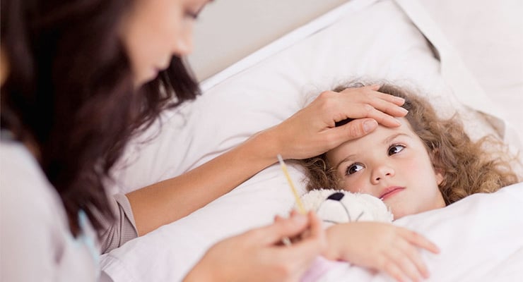 Madre tomando la temperatura de una niña enferma recostada en la cama