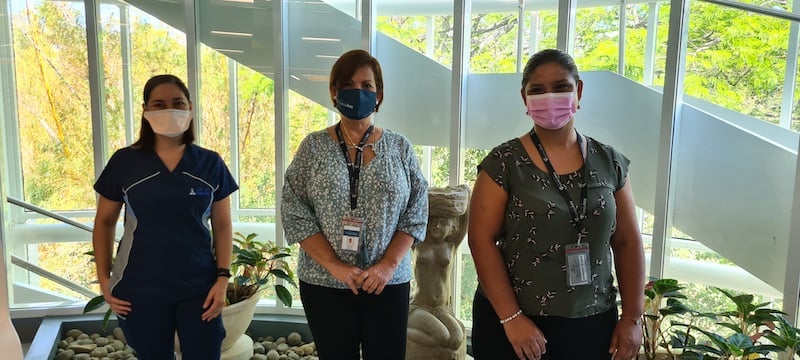 Tres mujeres, incluyendo personal médico con mascarillas, posan en unas escaleras iluminadas durante la campaña de salud en Santa Ana.