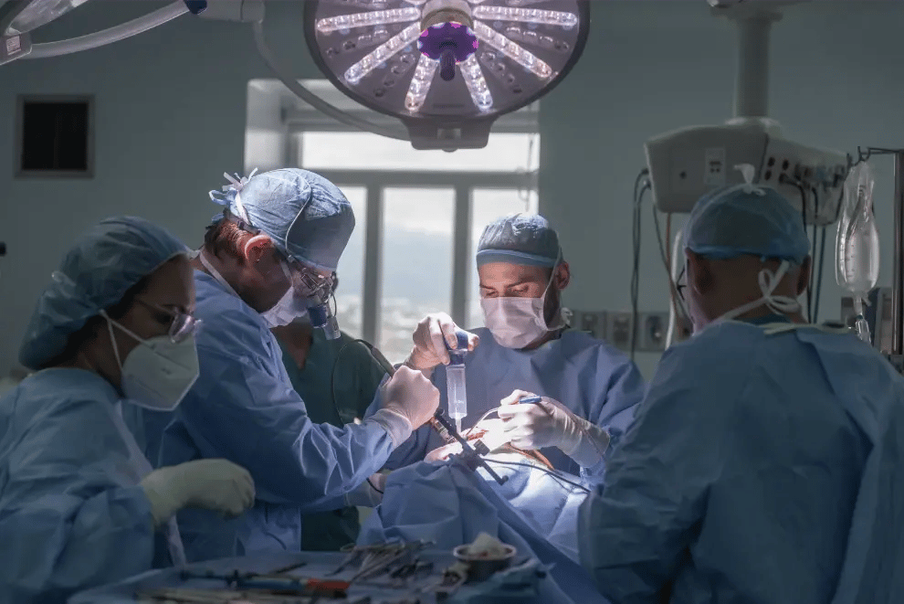 Equipo de cirujanos realizando una operación en quirófano bajo luz quirúrgica con instrumental médico.