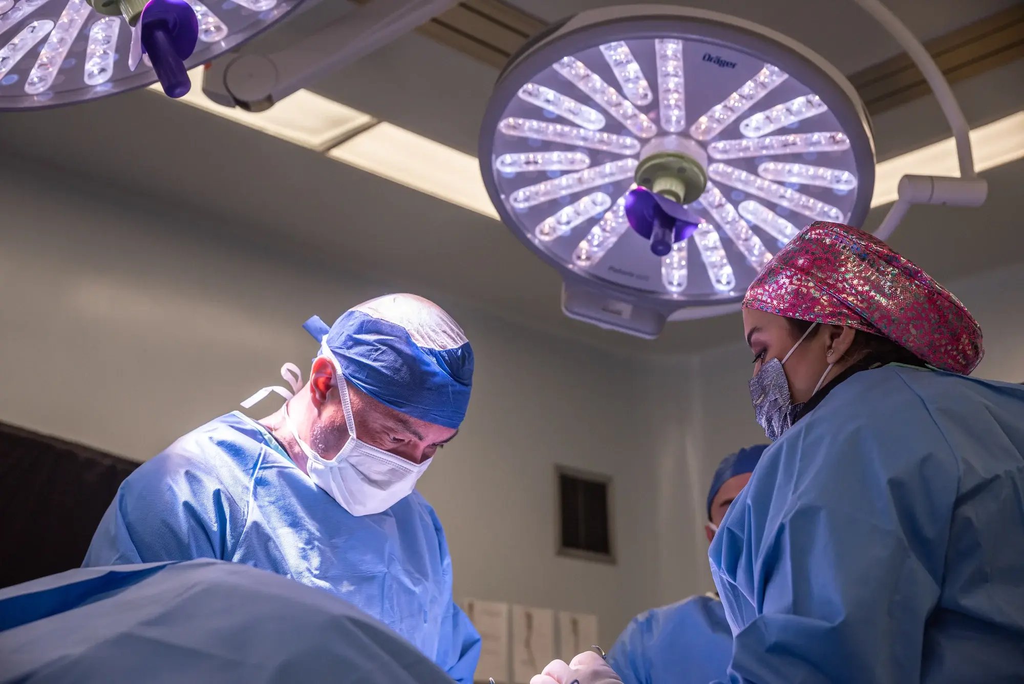 Equipo médico realizando una cirugía bajo luces quirúrgicas en una sala de operaciones. Equipo médico realizando una cirugía bajo luces quirúrgicas en una sala de operaciones.