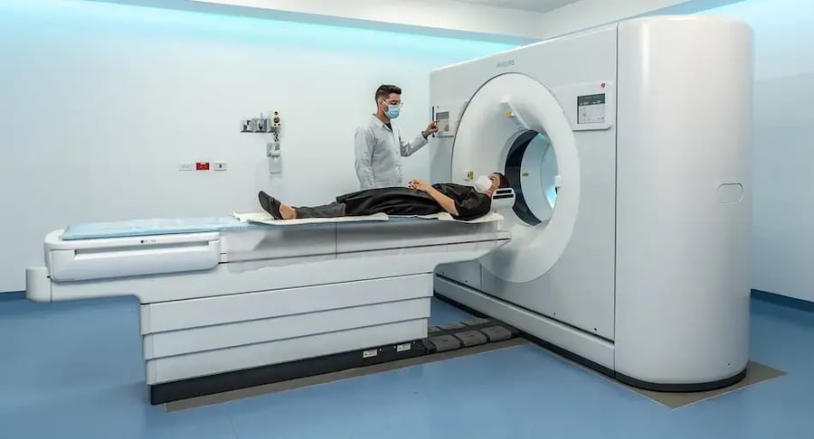 Paciente acostada en mesa de tomógrafo mientras un técnico opera el equipo médico.