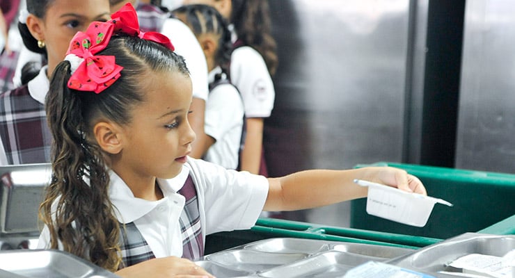 Niña estudiante recibiendo alimentos en el comedor escolar.