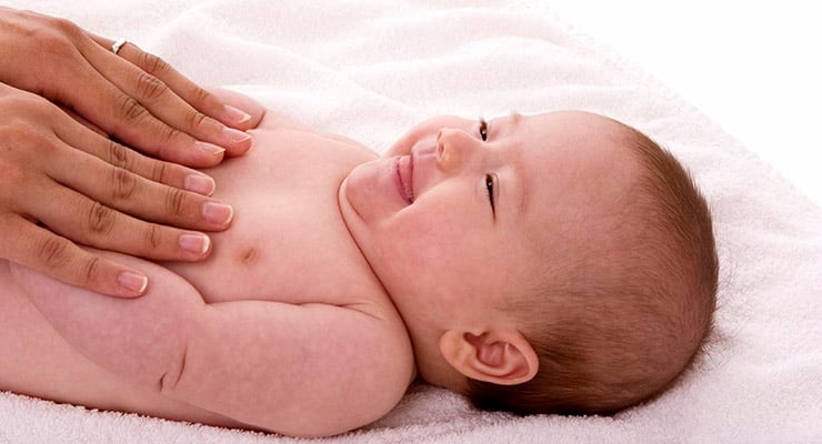 Bebé recién nacido acostado mientras un adulto apoya suavemente las manos sobre su abdomen