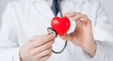 Un médico sosteniendo un pequeño corazón rojo con un estetoscopio, representando la medicina preventiva y el cuidado cardiovascular avanzado.