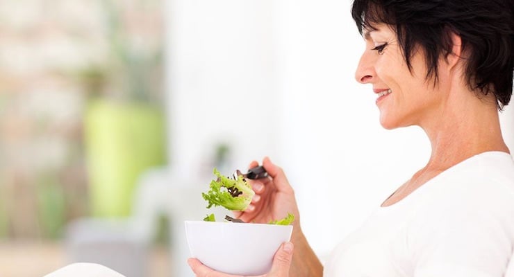 Mujer adulta comiendo ensalada en casa como parte de un estilo de vida saludable