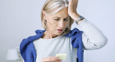 Mujer adulta mayor con expresión de preocupación y confusión mientras sostiene una nota adhesiva, representando la detección de fallos de memoria.