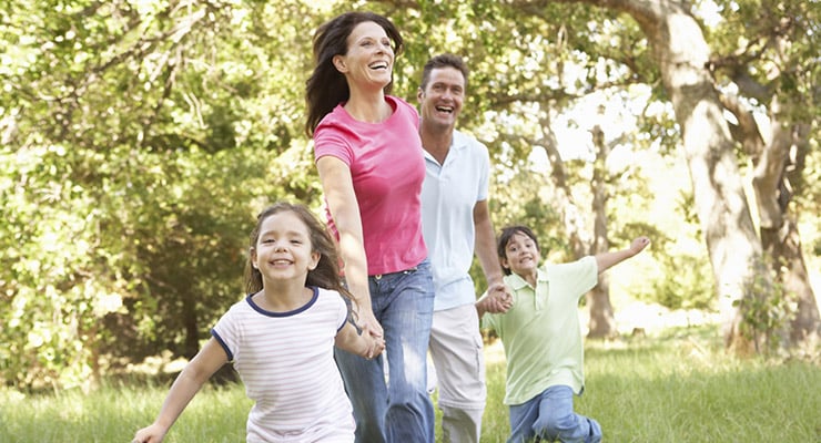 Familia caminando y sonriendo al aire libre en un parque con árboles
