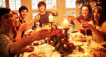 Grupo de personas brindando durante una cena navideña alrededor de una mesa con velas y comida