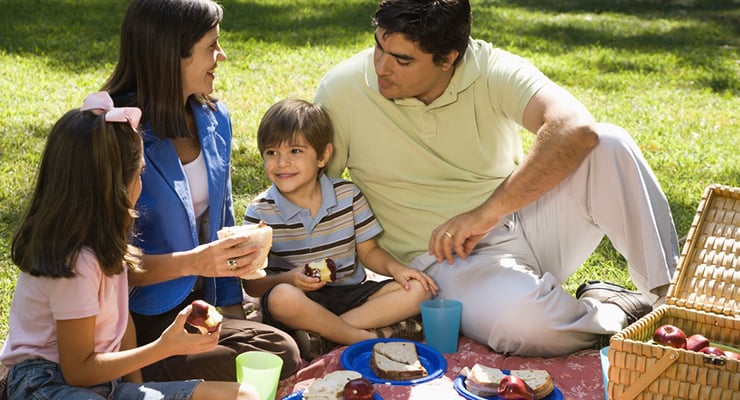 Familia sentada sobre el césped compartiendo comida durante un picnic al aire libre