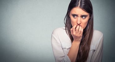 Mujer joven con expresión de temor y ansiedad, mordiéndose las uñas mientras mira con preocupación hacia un lado, ilustrando los síntomas de una fobia.