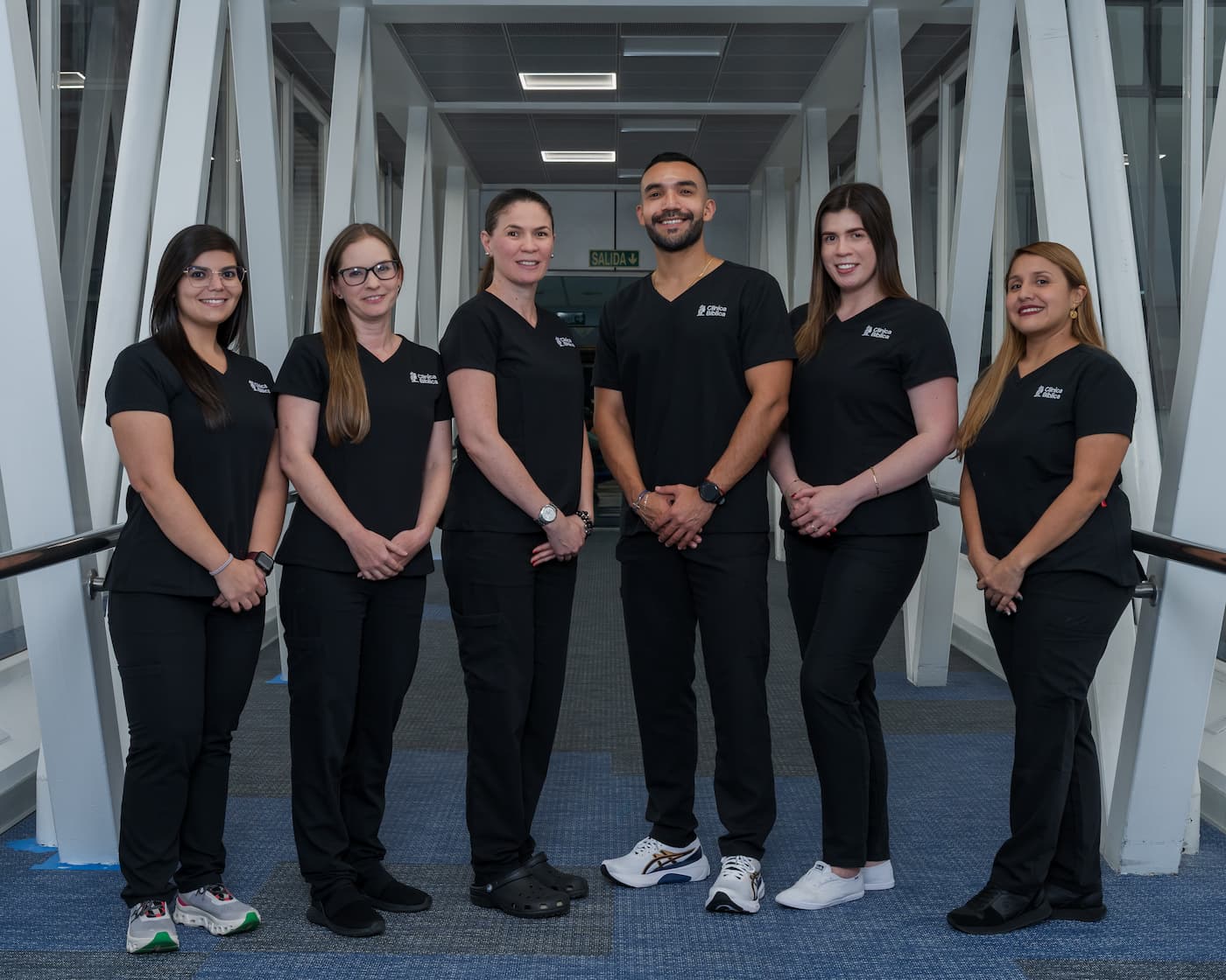 Foto del equipo de personal medico y profesionales de la salud vistiendo uniformes negros de Clinica Biblica, posando de pie en el pasillo de un hospital.