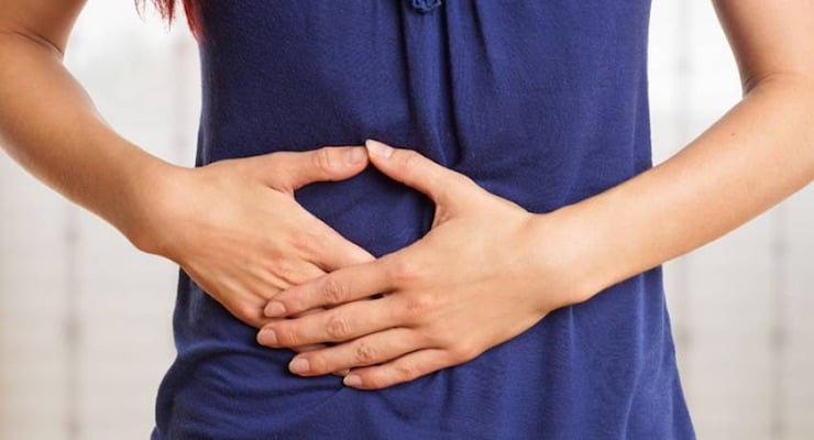 Mujer con manos sobre el abdomen por molestias gastrointestinales