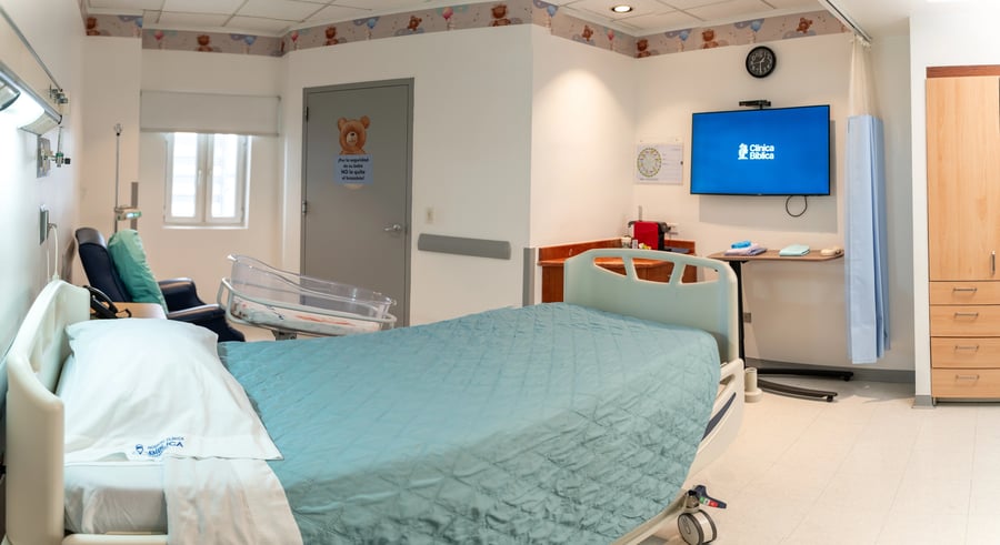 Habitación hospitalaria equipada con cama, cuna para bebé y pantalla de Clínica Bíblica