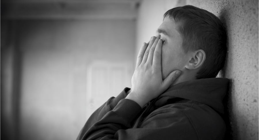 Hombre apoyado contra una pared con las manos cubriendo el rostro en señal de angustia emocional