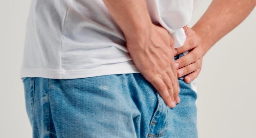 Primer plano de un hombre sujetándose la zona de la ingle con ambas manos debido a síntomas de dolor por hernia inguinal.