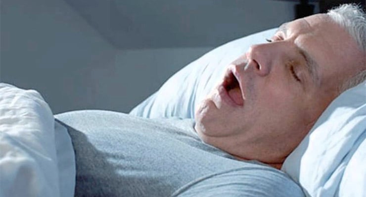 Hombre acostado en una cama durmiendo con la boca abierta